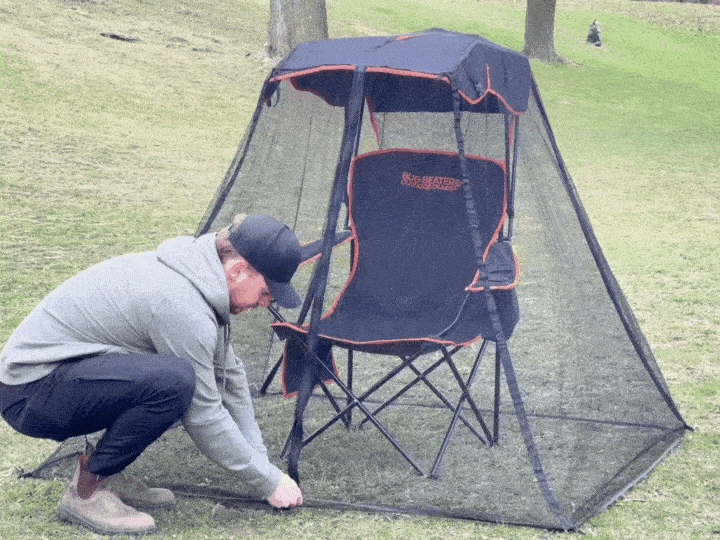 Man unzipping the bug netting and sitting in his Bug Beater chair, closing the netting behind him and taking a drink from a can in the mesh holder located on the right arm of the chair.